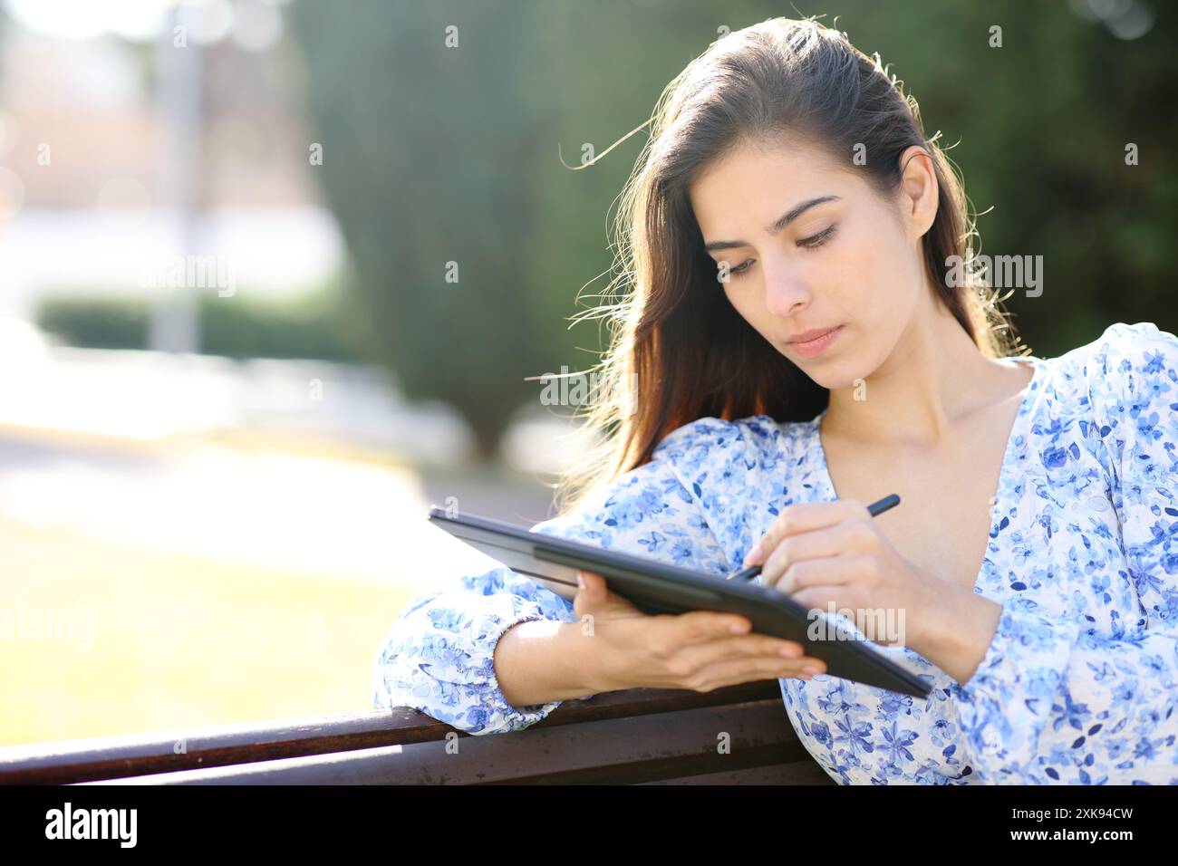 Frau, die auf einem Tablet mit digitalem Stift sitzt, sitzt in einem Garten Stockfoto