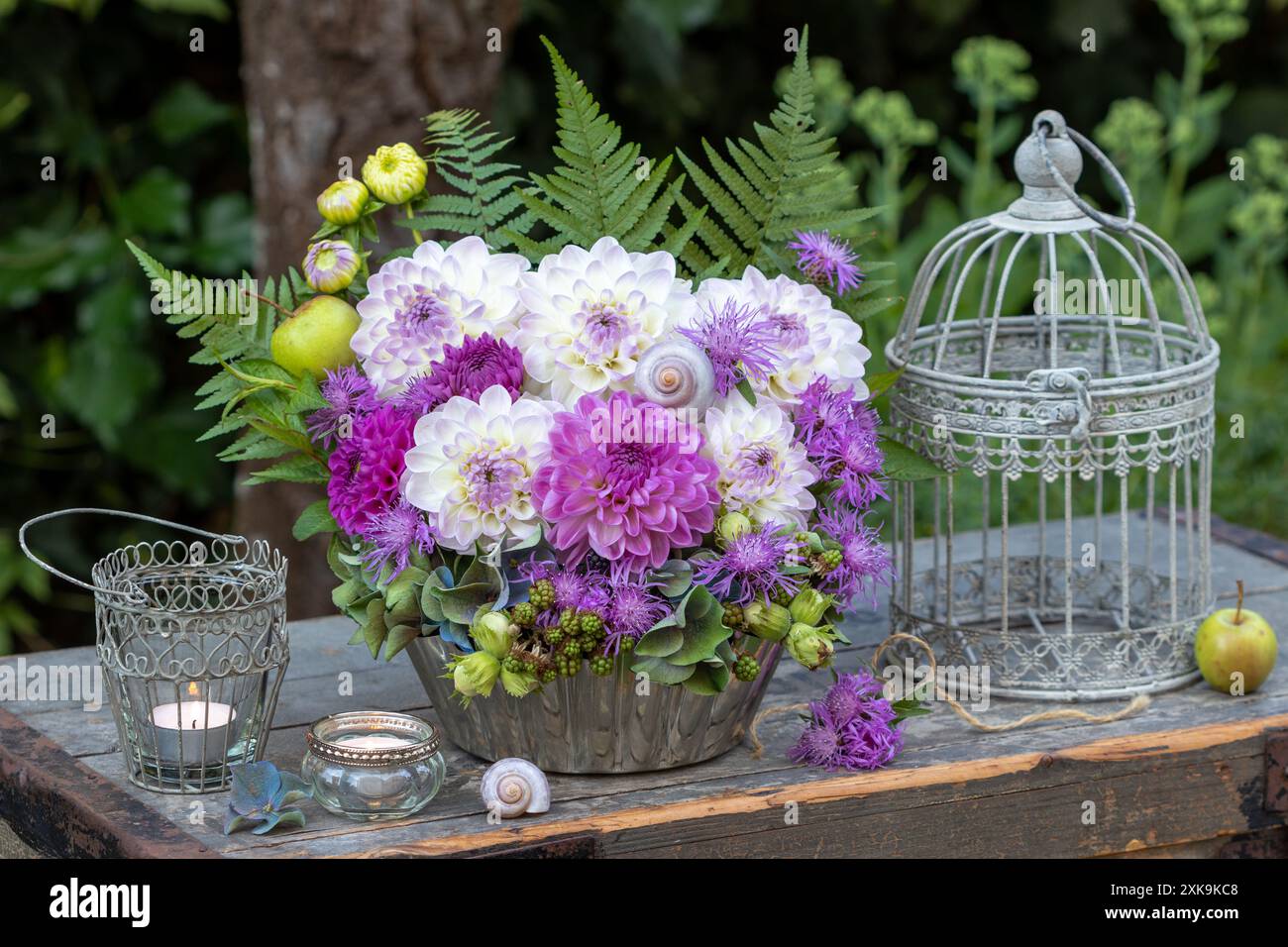 Gartendekoration mit Blumenanordnung von Dahlien, Wiesenkraut, Hortensie, Brombeeren, Haselnüssen, farnblätter, Vogelkäfig und Tischlaternen Stockfoto