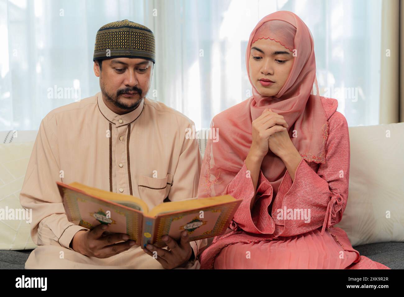 Asiatische muslimische Familie liest zu Hause den koran zusammen. Asiatisch-muslimischer Mann, der Ehefrau unterrichtet, Koran oder Koran im Wohnzimmer zu lesen Stockfoto