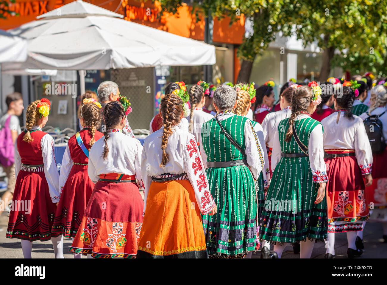 Bulgarische Frauen in traditioneller Volkskleidung gehen in die Stadt, bunte Röcke und Blusen mit Blumen im Haar Stockfoto