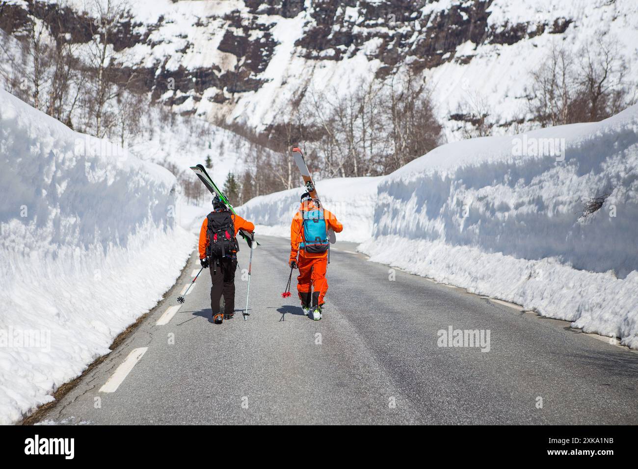 Zwei Skifahrer zu Fuß auf eine Straße zwischen zwei hohen Mauern der Schnee in der Nähe von Skigebiet auf Myrkdalen, Fjord, Norwegen Stockfoto
