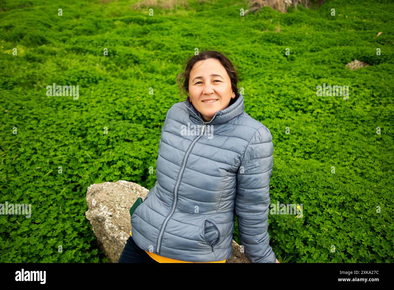 Frau in grauer Jacke lächelt auf grünem Gras Stockfoto