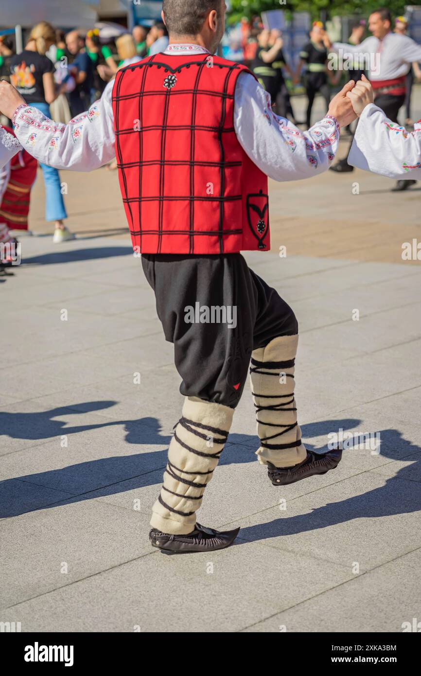 Männer und Frauen, beide tragen traditionelle bulgarische Kleidung, tanzen den Horo, einen kreisrunden Volkstanz Stockfoto