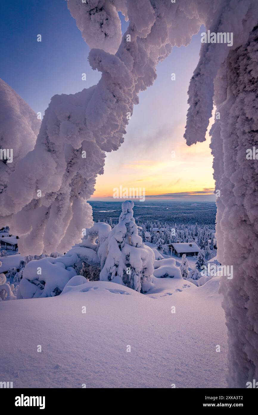 Schneebedeckte Berghütten in einem gefrorenen Wald bei Sonnenaufgang, Lappland, Finnland Stockfoto