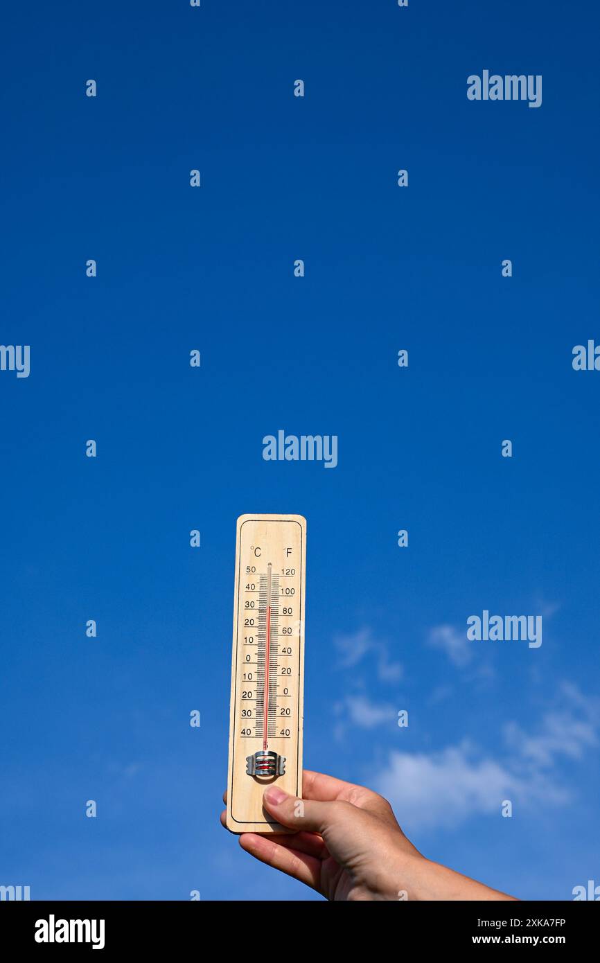 Holzthermometer mit hoher Temperatur an einem sonnigen Tag mit blauem Himmel und Wolken. Stockfoto