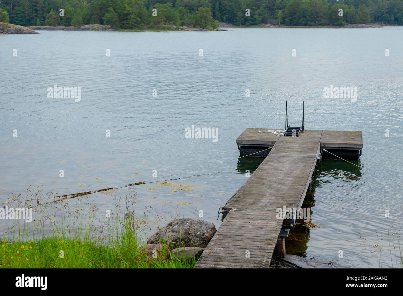 Hölzerne schwimmende Plattform mit Treppen an der Ostsee im Sommerurlaub in Finnland, Meer und Wald auf einem Hintergrund Stockfoto