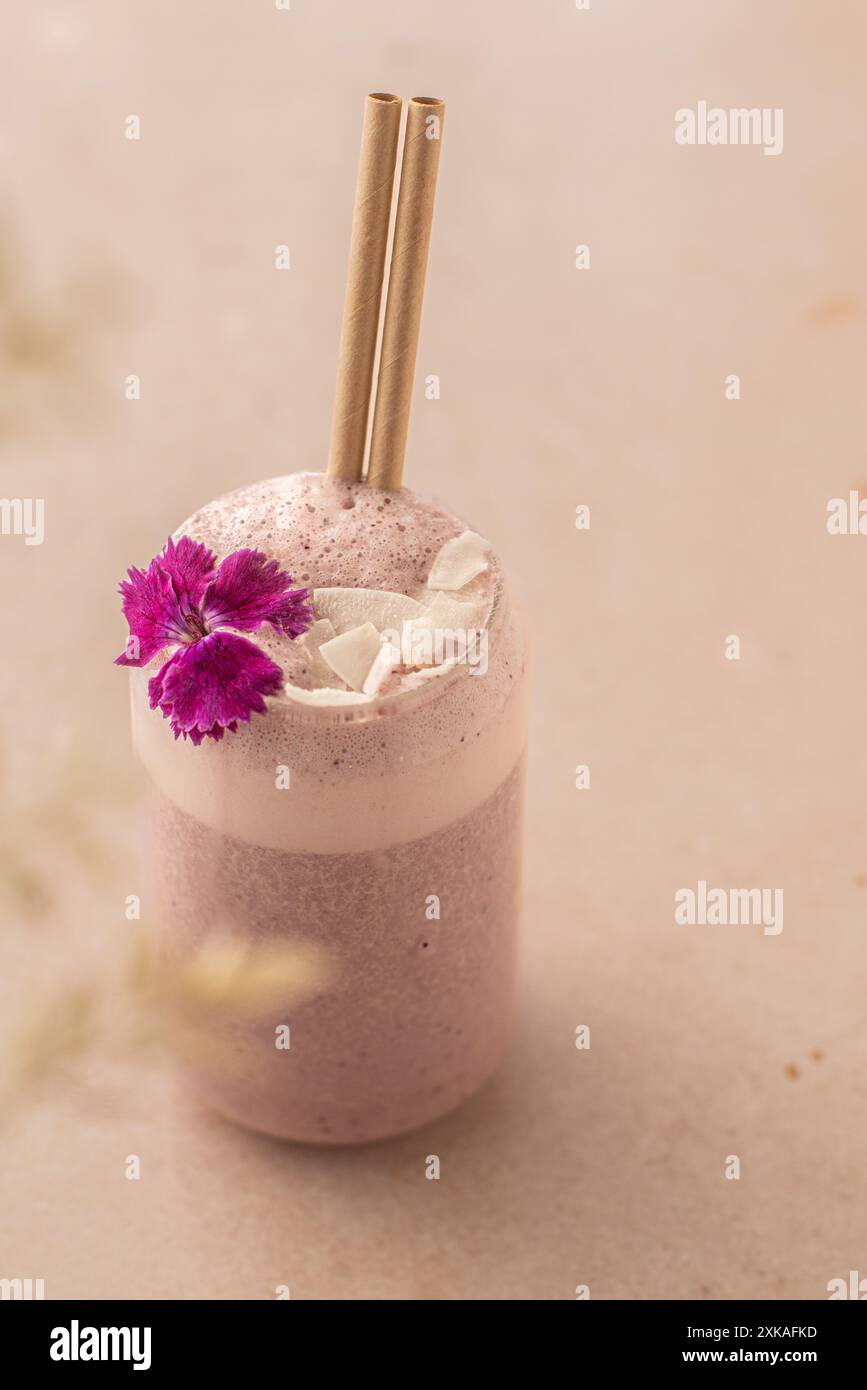 Veganer Smoothie mit Erdbeeren, dekoriert mit Kokosnuss und essbarer Blume auf einem Coffee Shop Tisch. Stockfoto