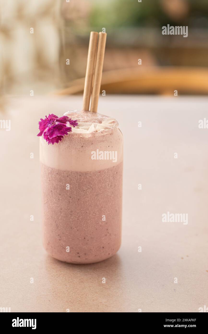 Veganer Smoothie mit Erdbeeren, dekoriert mit Kokosnuss und essbarer Blume auf einem Coffee Shop Tisch. Stockfoto