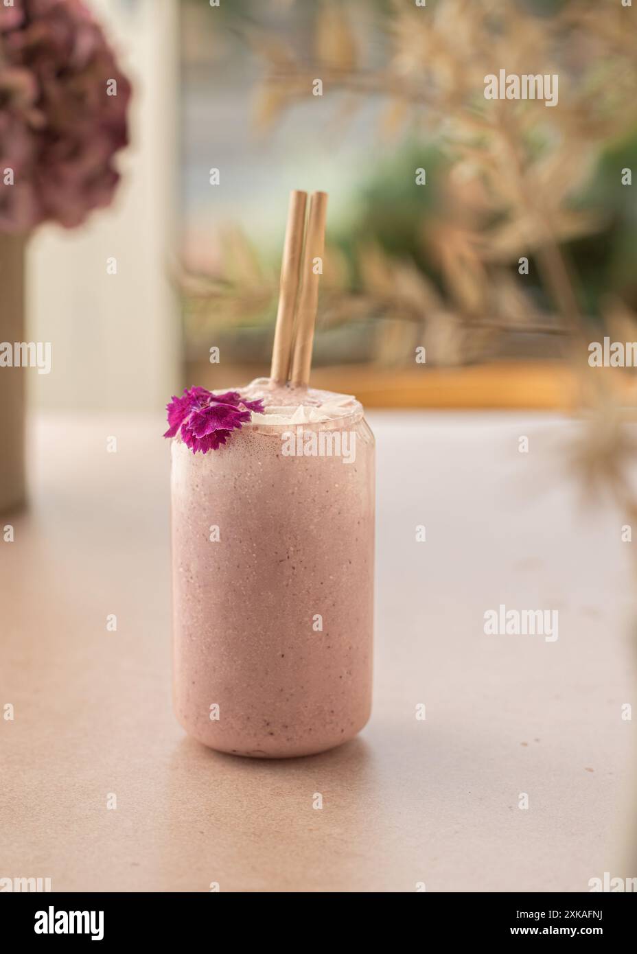 Veganer Smoothie mit Erdbeeren, dekoriert mit Kokosnuss und essbarer Blume auf einem Coffee Shop Tisch. Stockfoto