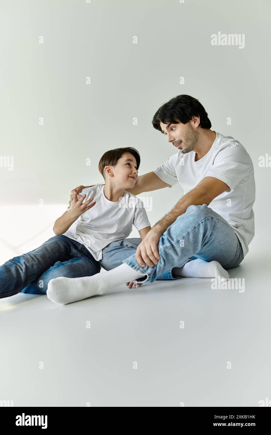 Ein Vater und ein Sohn sitzen zusammen auf einem weißen Boden und führen ein Gespräch. Stockfoto