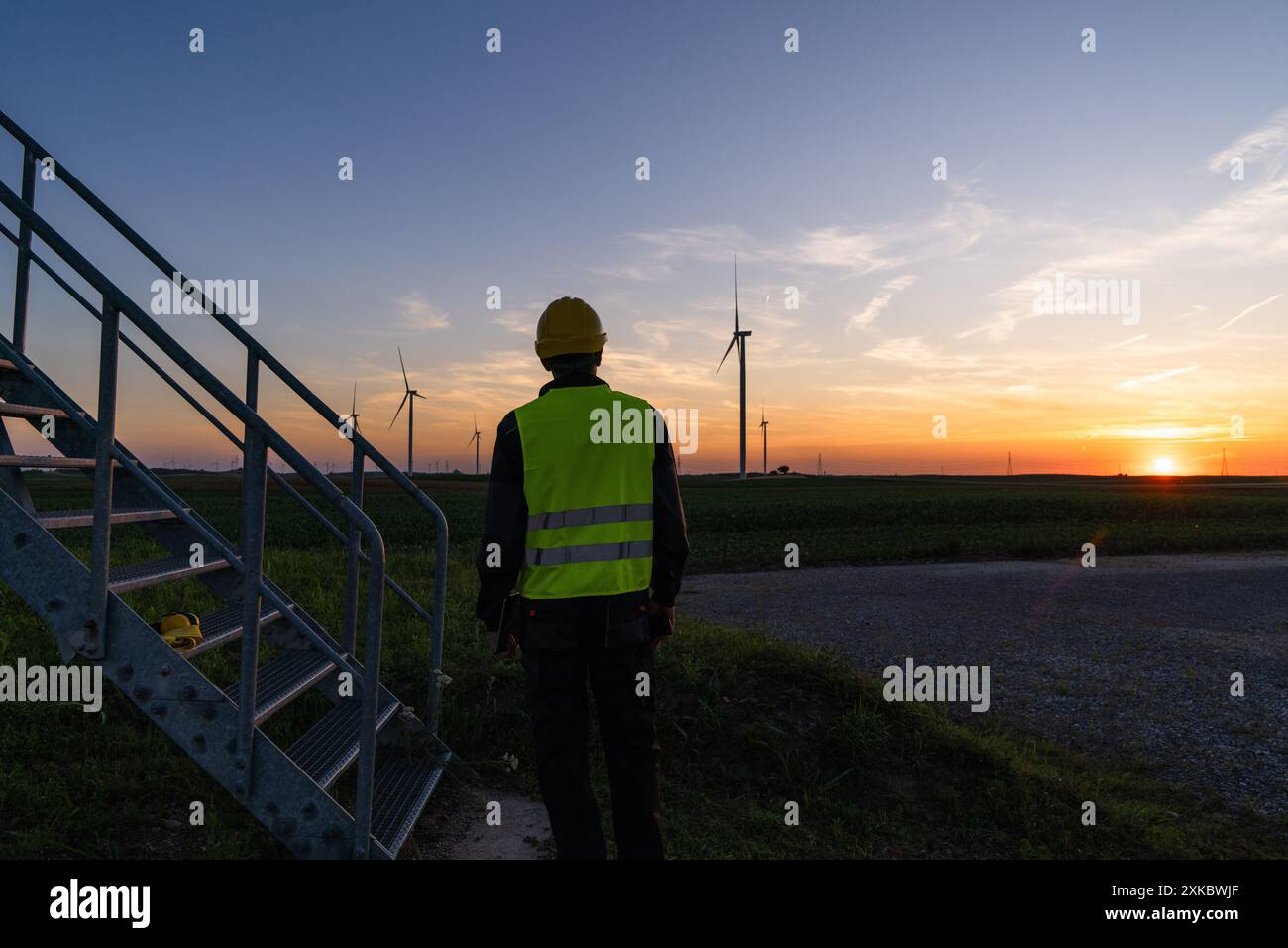 Arbeiter schaut sich Windräder bei Sonnenuntergang an. Stockfoto