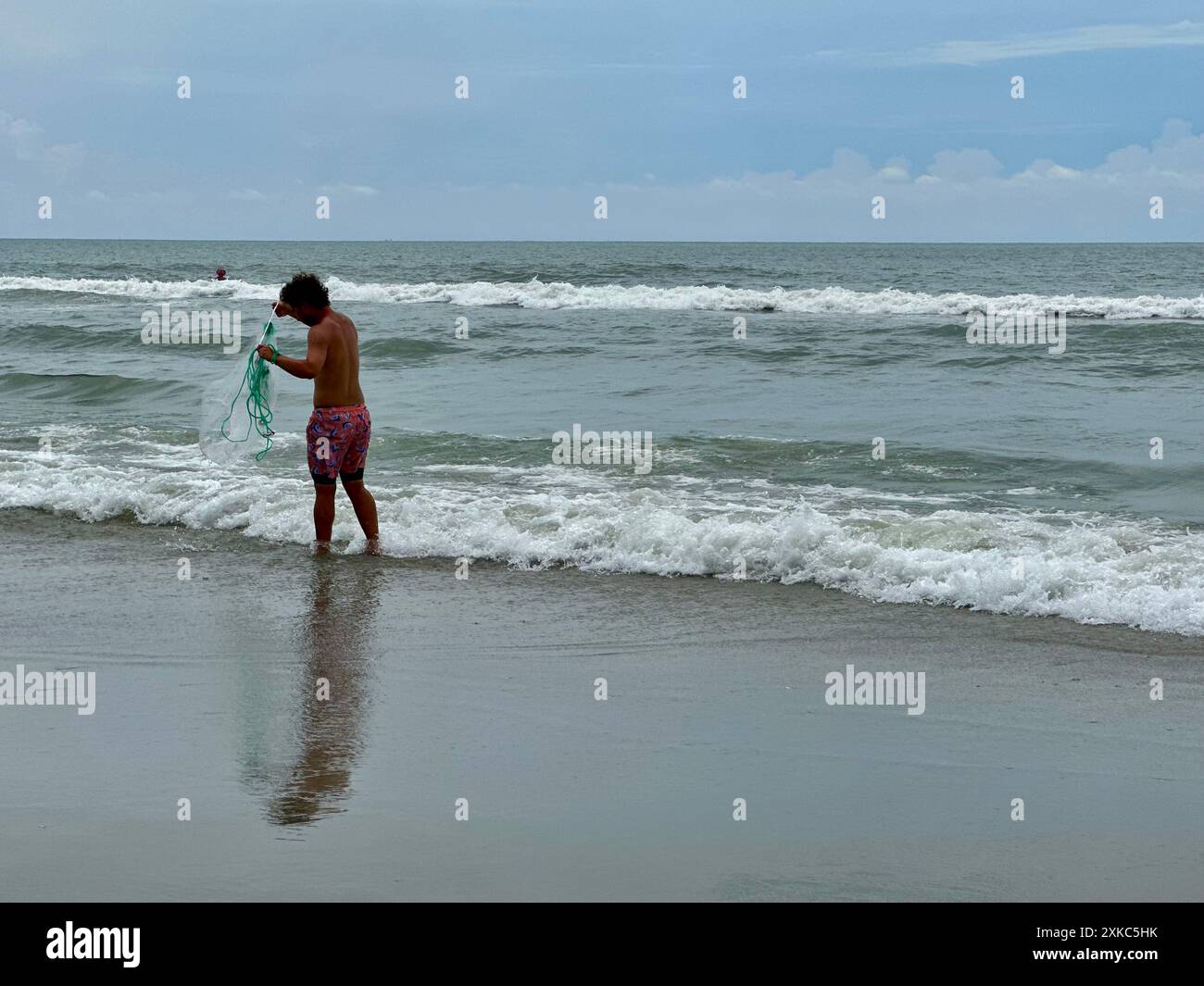 Ein junger Mann steht am Rand des Ozeans und wirft ein Netz für Köder an den trüben Ufern von North Myrtle Beach, South Carolina. Stockfoto