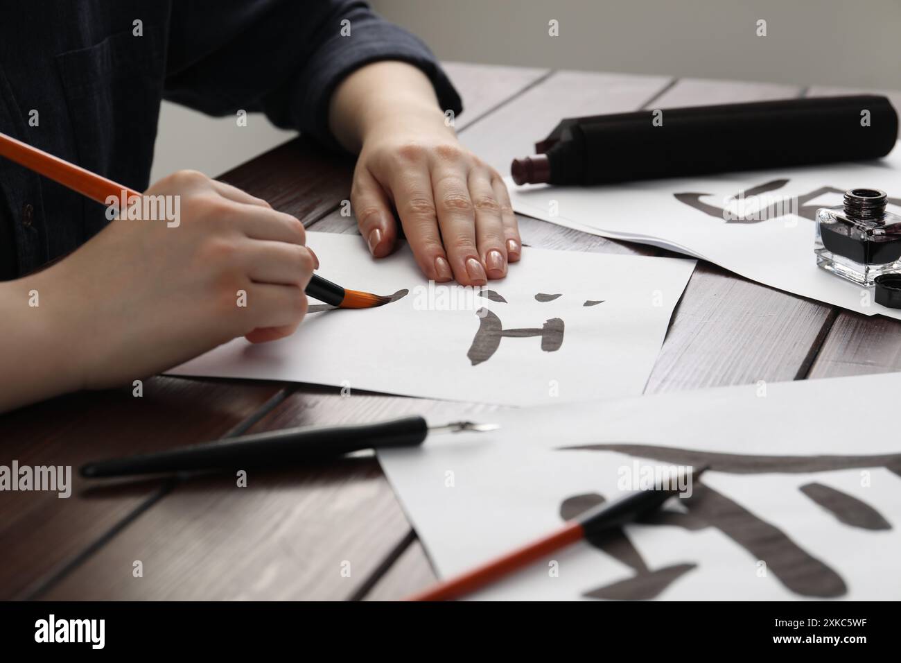 Kalligraphie. Frau mit Pinsel und Tintenfass, die chinesische Hieroglyphen auf Papier auf Holztisch schreibt, Großaufnahme Stockfoto