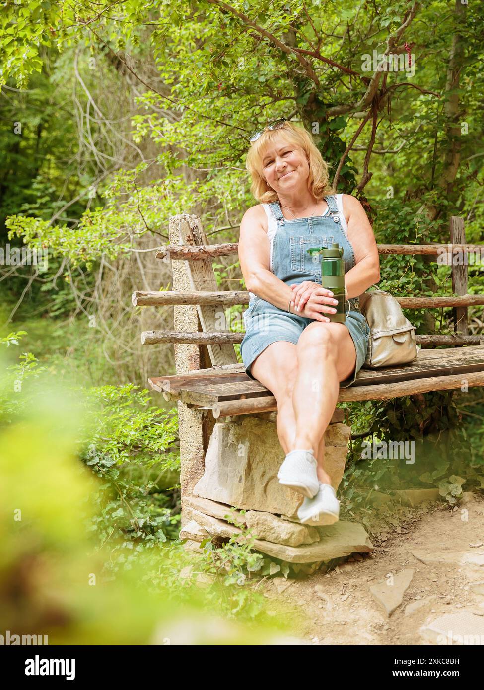 Frau, die Wasser aus wiederverwendbarer Trinkflasche im Wald trinkt Stockfoto