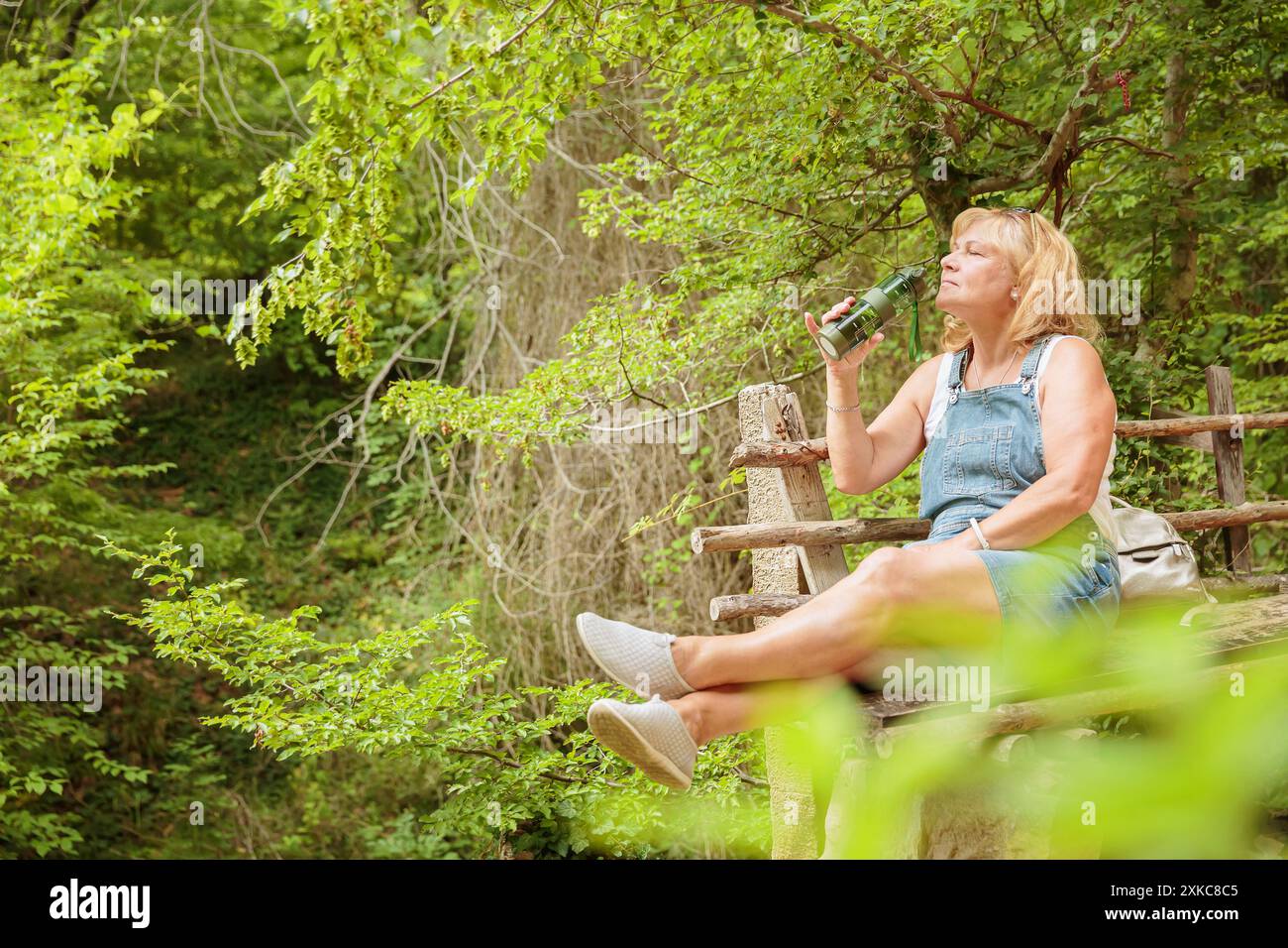 Frau, die Wasser aus wiederverwendbarer Trinkflasche im Wald trinkt Stockfoto