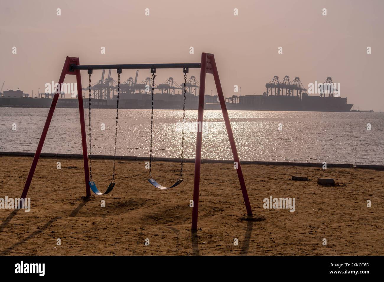 Der Kinderspielplatz mit Schaukeln an der Küste des Roten Meeres mit Blick auf den islamischen Hafen von Dschidda in Saudi-Arabien mit den Seehafenkranichen. Stockfoto