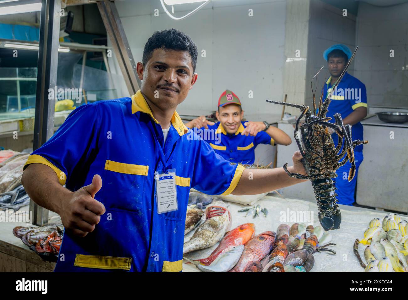 Der glückliche saudische Fischverkäufer auf dem Jeddah Fischmarkt, der Hummer und Daumen oben am Fischstand in Saudi-Arabien zeigt. Stockfoto