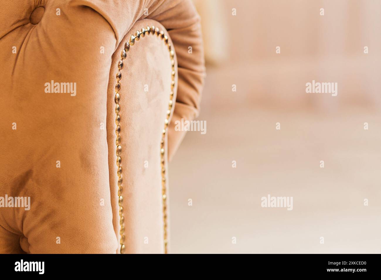 Nahaufnahme einer beigefarbenen Sofa-Armlehne mit goldener Nagelkopfverkleidung, die luxuriöse Möbeldetails in einem gemütlichen Zimmer hervorhebt. Stockfoto