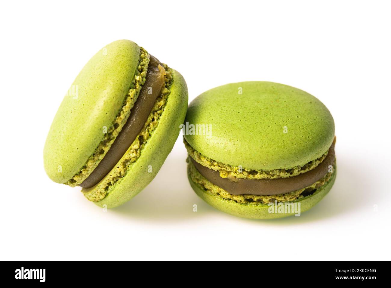 Zwei grüne Macarons mit cremiger Pistazienfüllung sind auf weißem Hintergrund angeordnet. Die Makronen sind leicht unscharf, wodurch ein weiches und eth entsteht Stockfoto