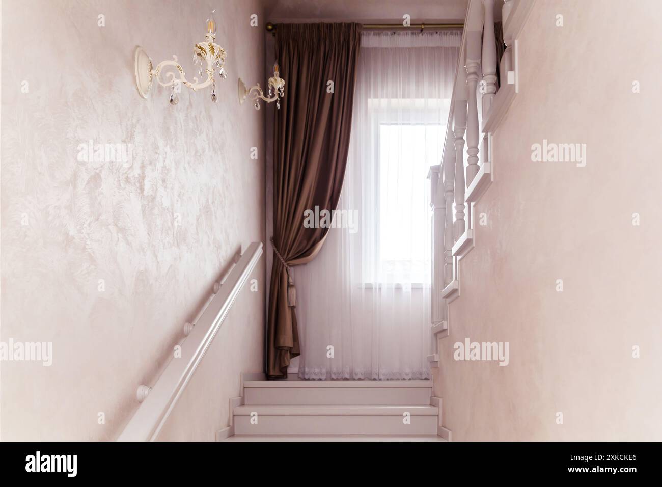 Treppe mit weißem Holzgeländer, beigefarbenen Wänden und einem braunen Vorhang am Fenster. Stockfoto