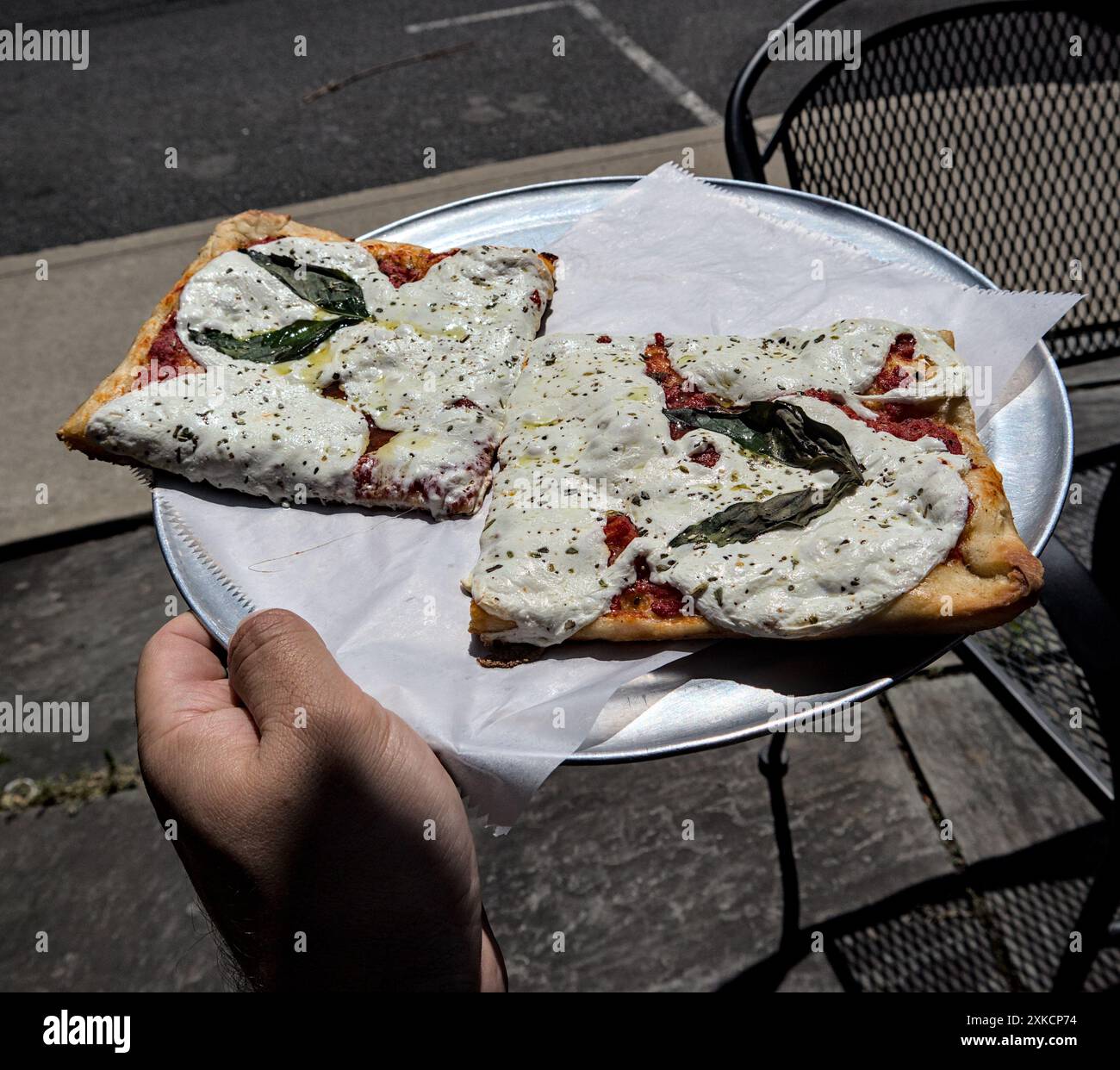 Zwei quadratische Scheiben sizilianischer Pizza (frische weiße Mozzarella-Basilikumblätter, dünne Kruste) auf rundem Tablett mit Pergamentpapier (italienische Küche) roter peppe Stockfoto