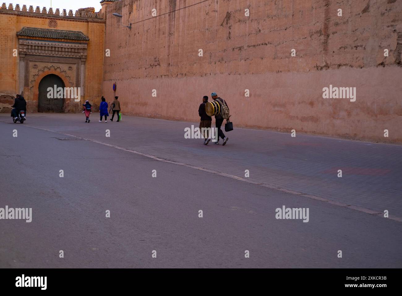 Die Menschen laufen entlang der hohen Mauer Red City Marrakesch, beeilen sich über Geschäfte, authentische afrikanische Stadtlandschaft, tägliche Aktivitäten und Interaktionen, die die Menschen leben Stockfoto