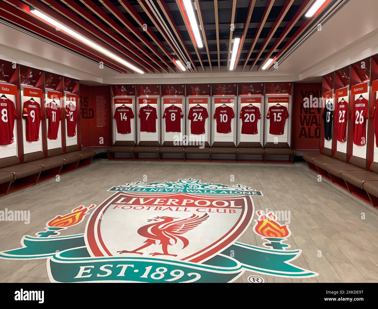 Der Umkleideraum des FC Liverpool bietet Spielertrikots, die ordentlich mit dem Vereinsemblem auf dem Boden angeordnet sind. Stockfoto