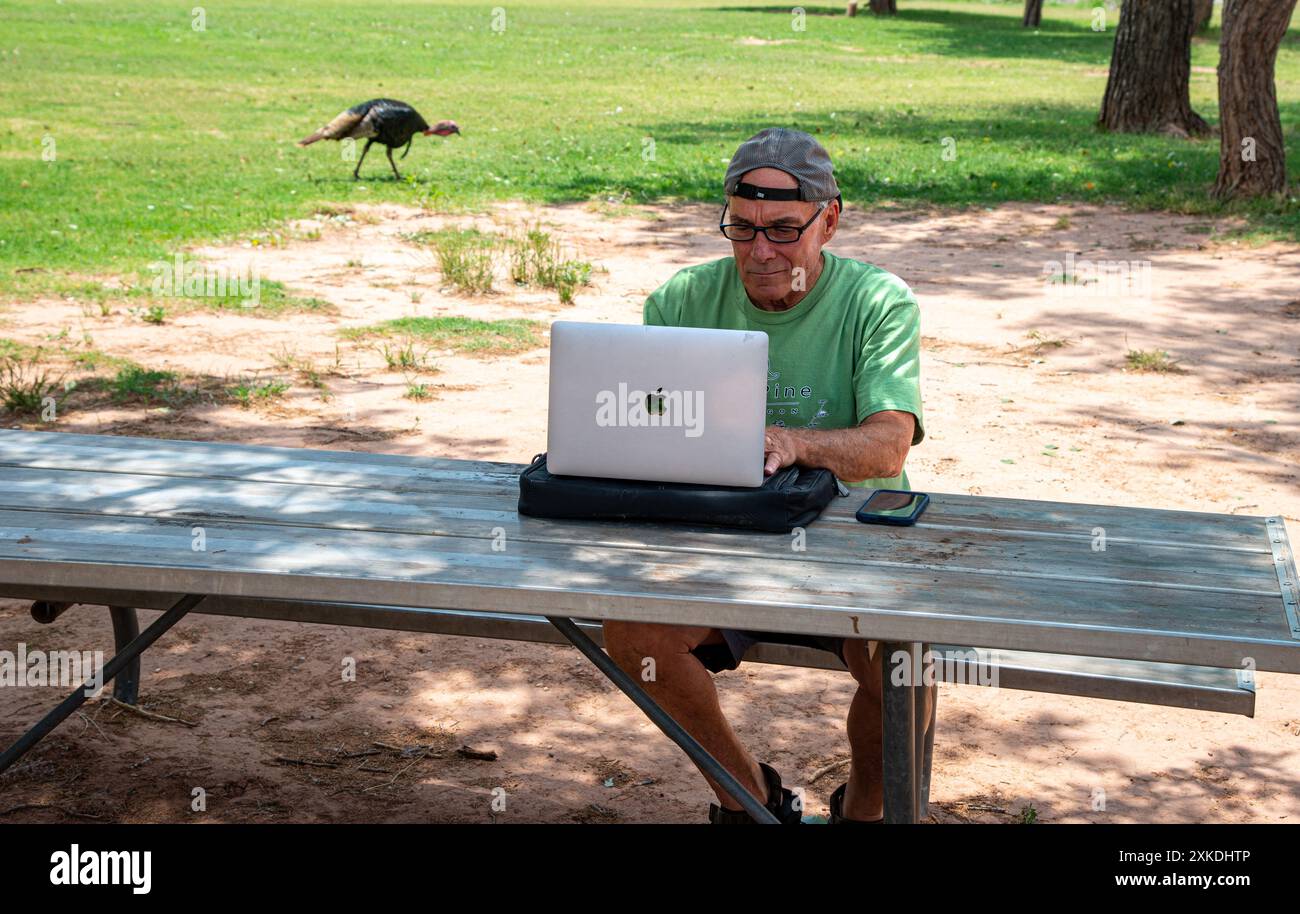 Ein Mann, der am Mac-Computer arbeitet, an einem Picknicktisch im Palo Duro Canyon State Park, Texas Stockfoto