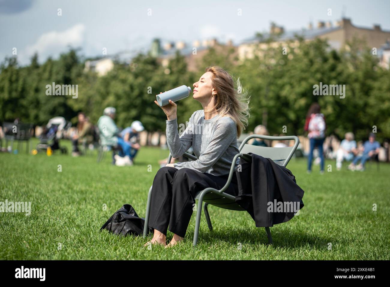 Dehydratation und Hitzschlag-Prophylaxe. Frau trinkt Wasser, sitzt am Sommertag in einer Liege im Park Stockfoto