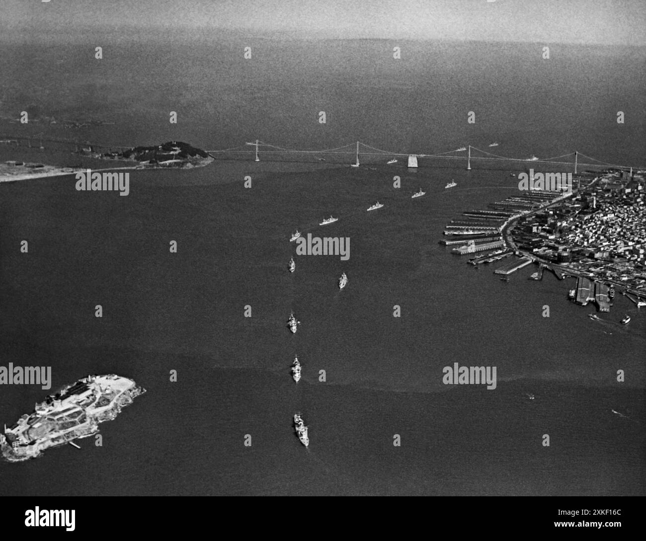 San Francisco, Kalifornien 28. Mai 1937 nachdem die Schiffe der United States Pacific Fleet in einer einzigen Datei unter der Golden Gate Bridge vorbeigefahren waren, dampften sie in die San Francisco Bay, um dort die Eröffnung der Golden Gate Bridge zu feiern. Dieses Bild zeigt die Schiffe in der Bucht, mit der San Francisco/Oakland Bay Bridge im Hintergrund und Alcatraz Island, dem Gefängnis der Vereinigten Staaten, im Vordergrund. Stockfoto