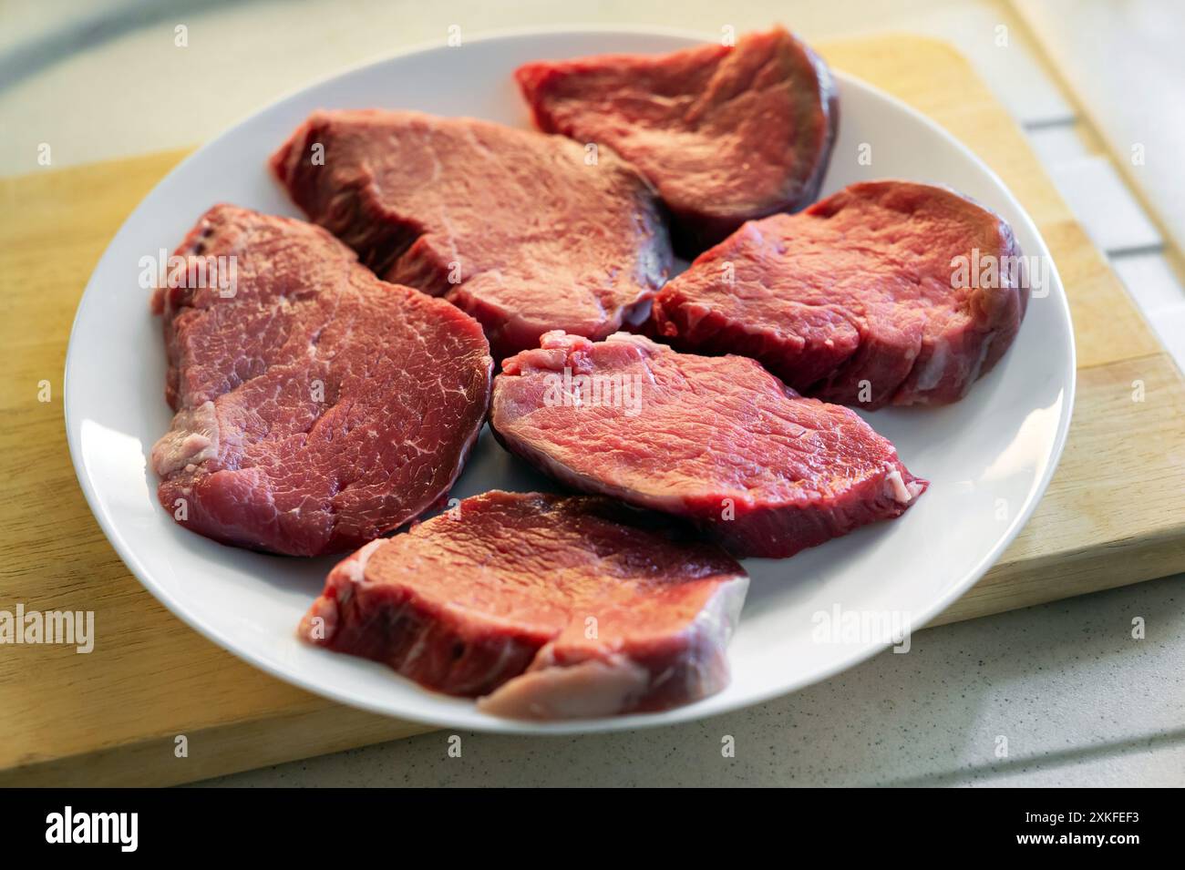 Mehrere rohe Rindersteaks werden auf einem weißen Teller zum Würzen und Grillen zubereitet Stockfoto