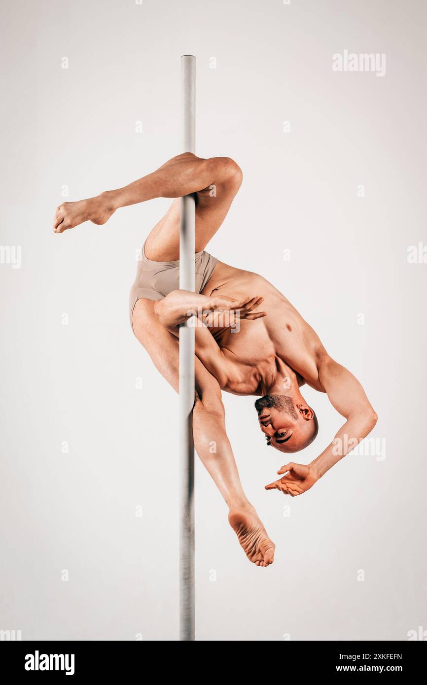 Der muskulöse Mann hält anmutig eine Pole-Dance-Pose und zeigt Kraft und Flexibilität Stockfoto
