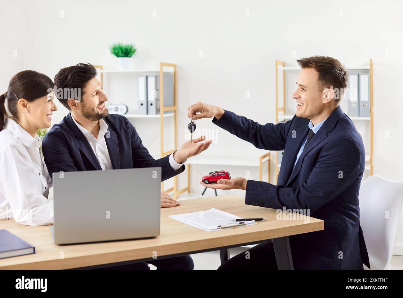 Autoverkäufer im Büro, die Schlüssel an Paare übergeben, Nahaufnahme Stockfoto