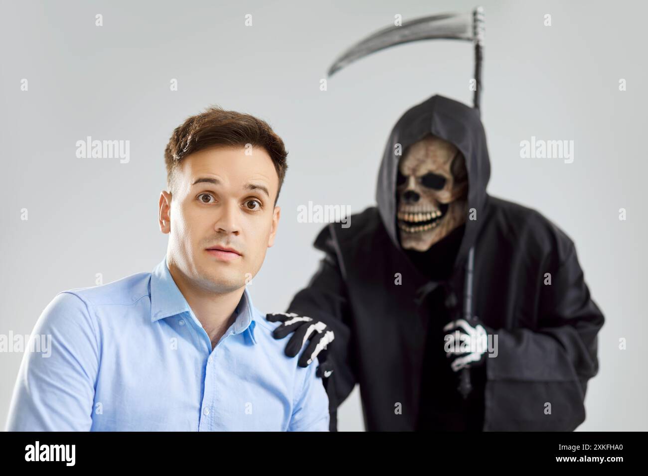 Grimmiger Sensenmann des Todes mit Sensenschulter, der sich an ein neues Opfer anschließt, junger Mann in Todesangst, stirbt Stockfoto