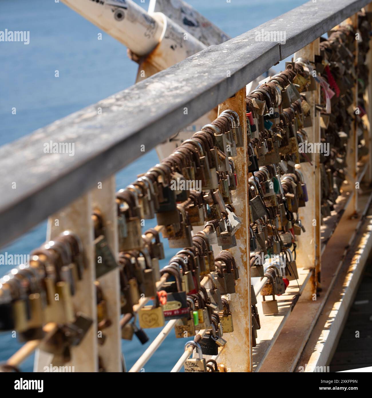 Zahlreiche Liebesschlösser, die an einem verrosteten Brücken-Geländer mit Blick auf das Meer befestigt sind, symbolisieren ewige Liebe und Hingabe. Stockfoto