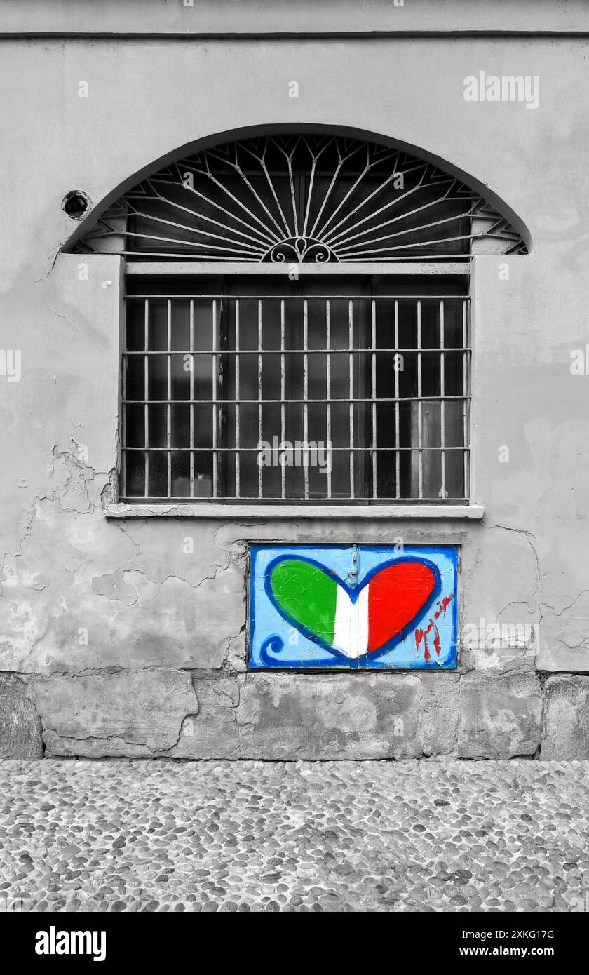 Schwarzweiß mit selektiver Farbe. Straßenkunst, die ein Herz mit den Farben der italienischen Flagge an der Gaskappe eines alten Hauses in Mailand, Italien, darstellt Stockfoto