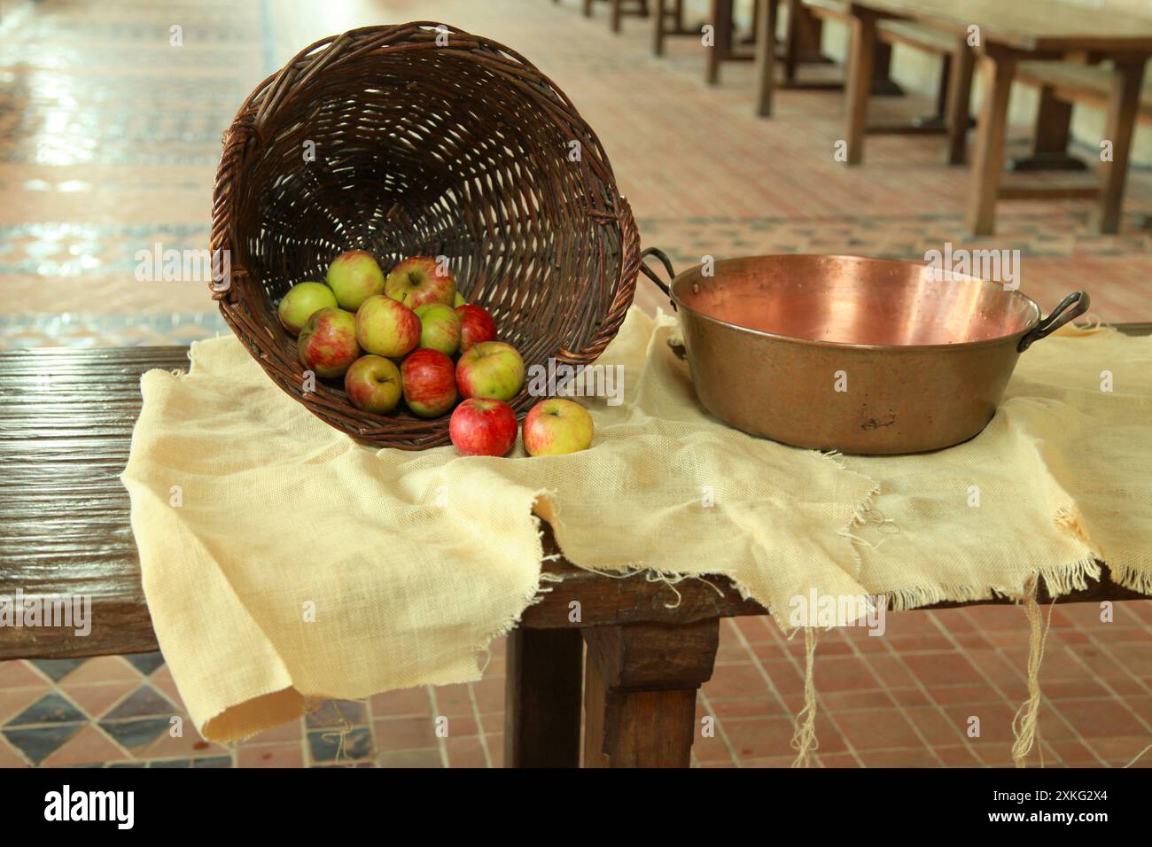 Stillleben mit einem Korb gefüllt mit Äpfeln und einem Kupferbecken, beide auf einem Leinen auf einem Tisch verteilt. Stockfoto