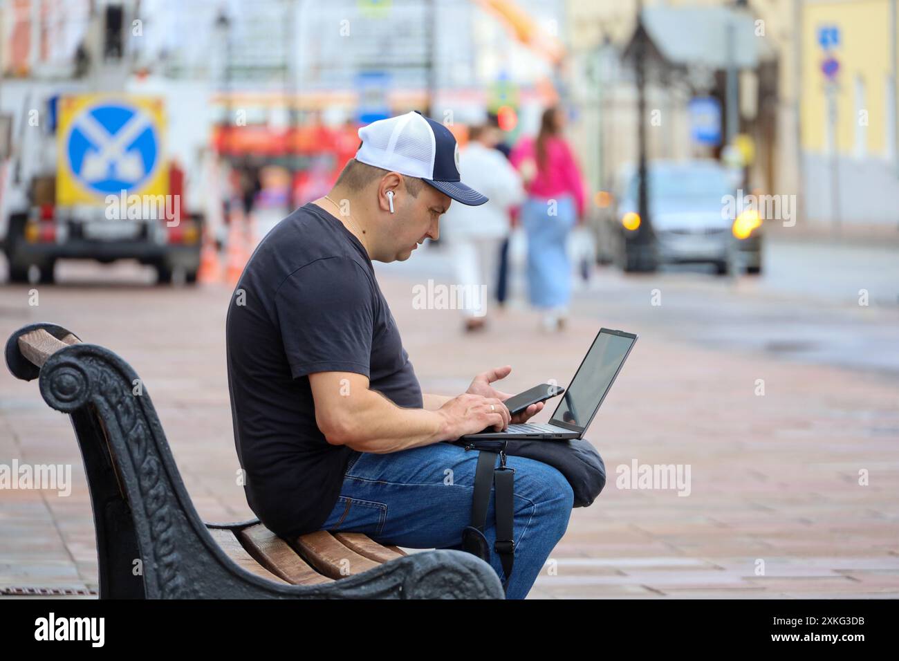 Mann, der mit Laptop und Smartphone auf der Straßenbank sitzt. Leben in der Sommerstadt, Online-Kommunikation und Fernarbeit Stockfoto