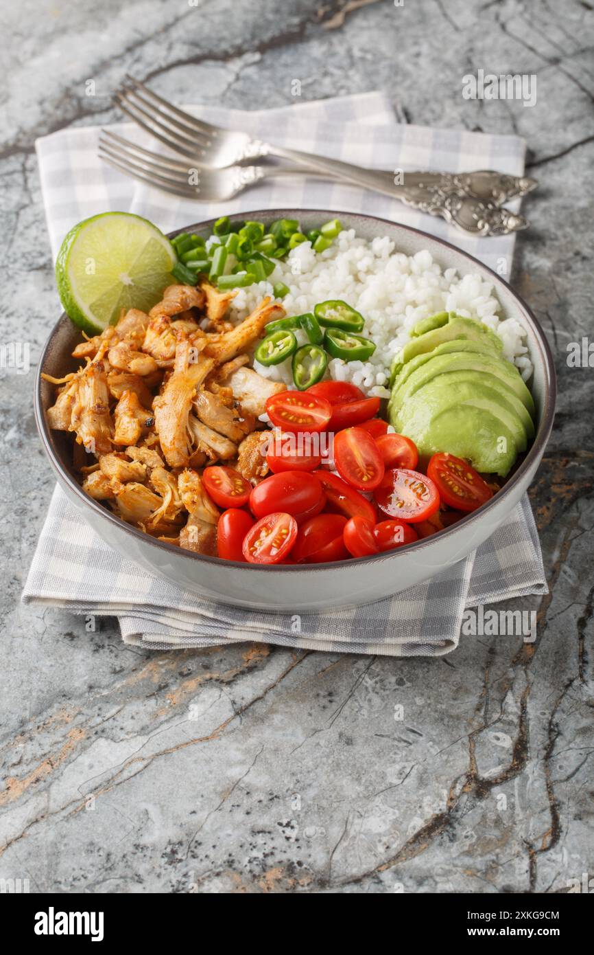 Mexikanische Reisschale mit Hühnchen-Carnitas, Kirschtomaten, Avocado, Paprika aus nächster Nähe auf dem Tisch. Vertikal Stockfoto