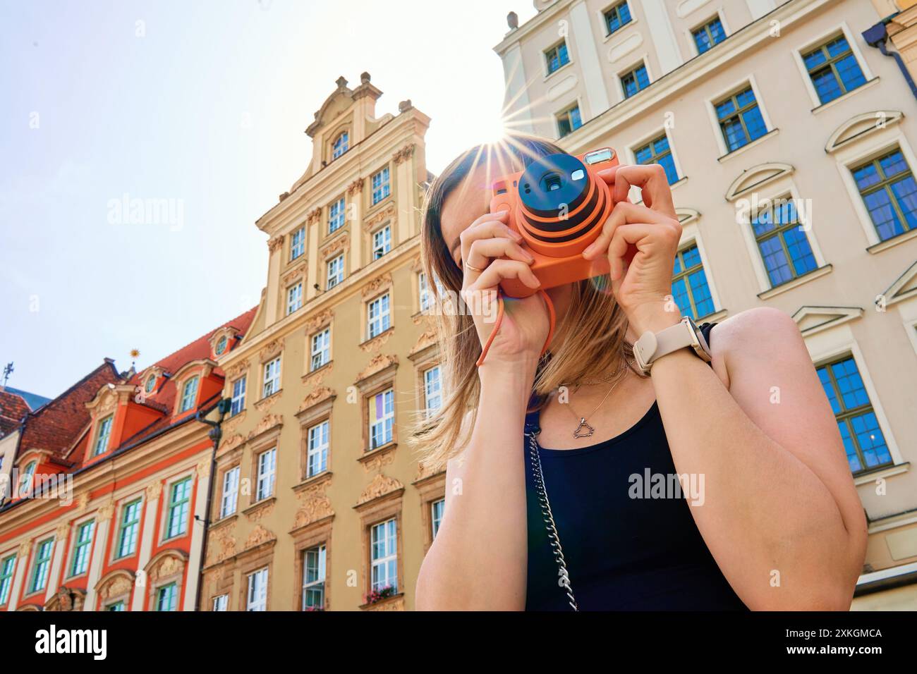 Frau, die an sonnigen Tagen Fotos von historischen europäischen Gebäuden macht, wobei Sonnenlicht einen Sterneneffekt über die Kamera erzeugt. Weibliche Touristen fängt Erinnerung ein Stockfoto