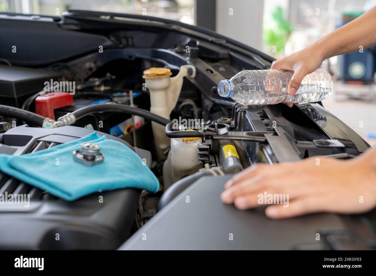 Eine junge Frau füllt den Kühler des Autos mit Wasser und führt eine Fahrzeugwartung durch Stockfoto