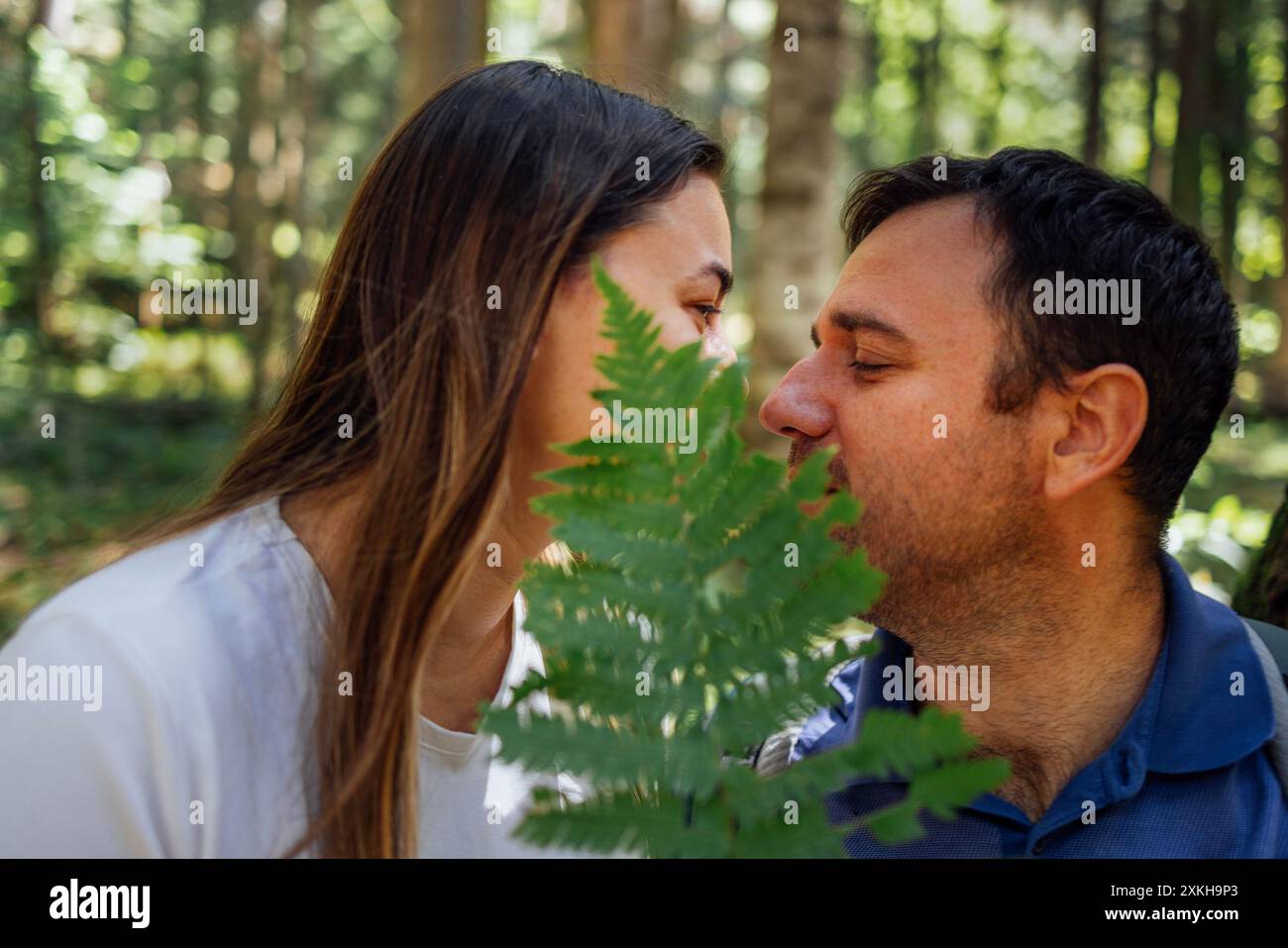 Ein Nahporträt einer charmanten Frau und eines Mannes mit einem Farn im Wald. Ein verliebtes Paar versteckt sich unter einem grünen Blatt im Wald. Glücklich Stockfoto