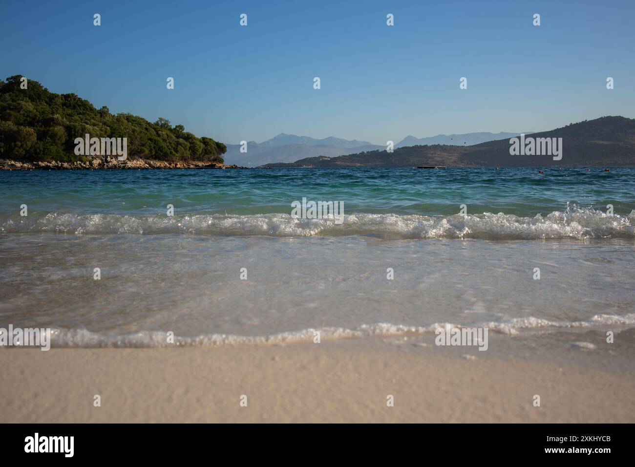 Vormittagslandschaft der Sandküste mit dem Ionischen Meer und der Insel Ksamil in Südalbanien. Albanische Landschaft mit Wasser und Bergen während des Sommervormittags. Stockfoto