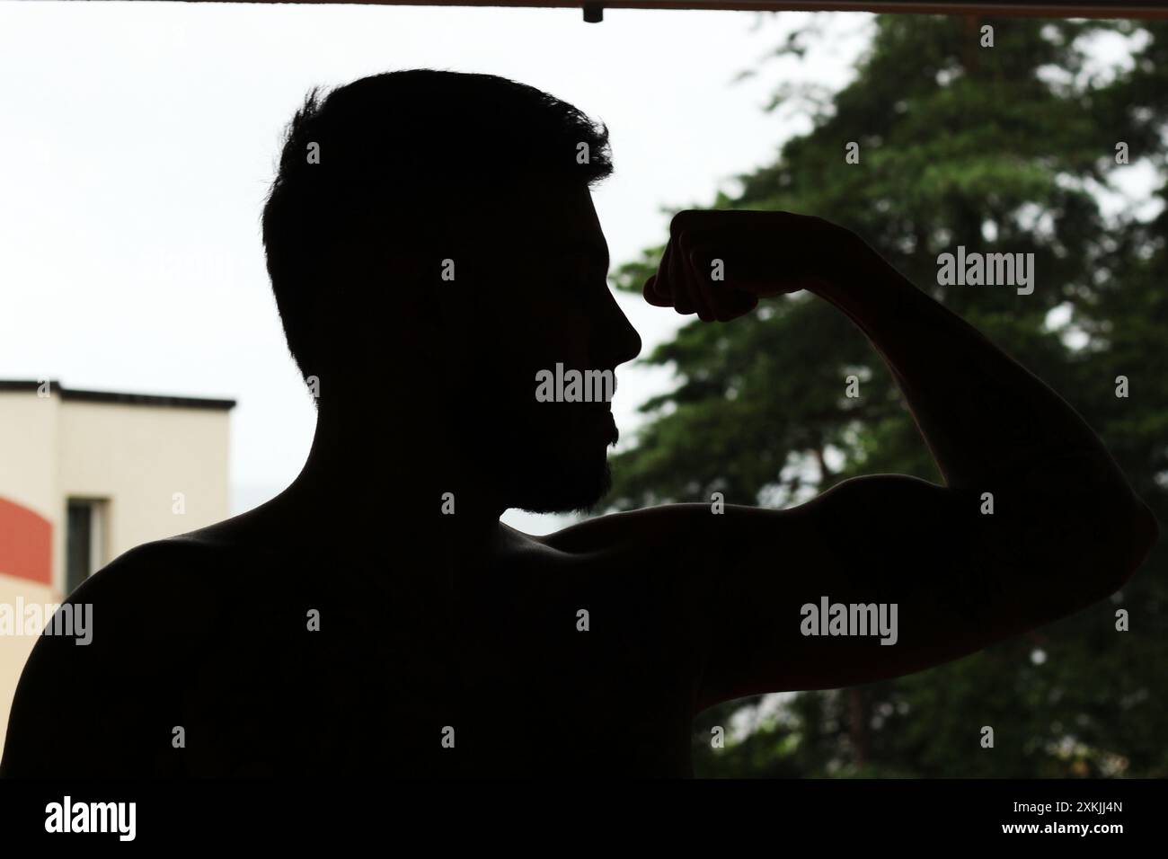 Ein kraftvolles Bild mit der Silhouette eines jungen muskulösen Mannes, der seinen Bizeps beugt. Perfekt für Themen rund um Fitness, Kraft und Bodybuildin Stockfoto
