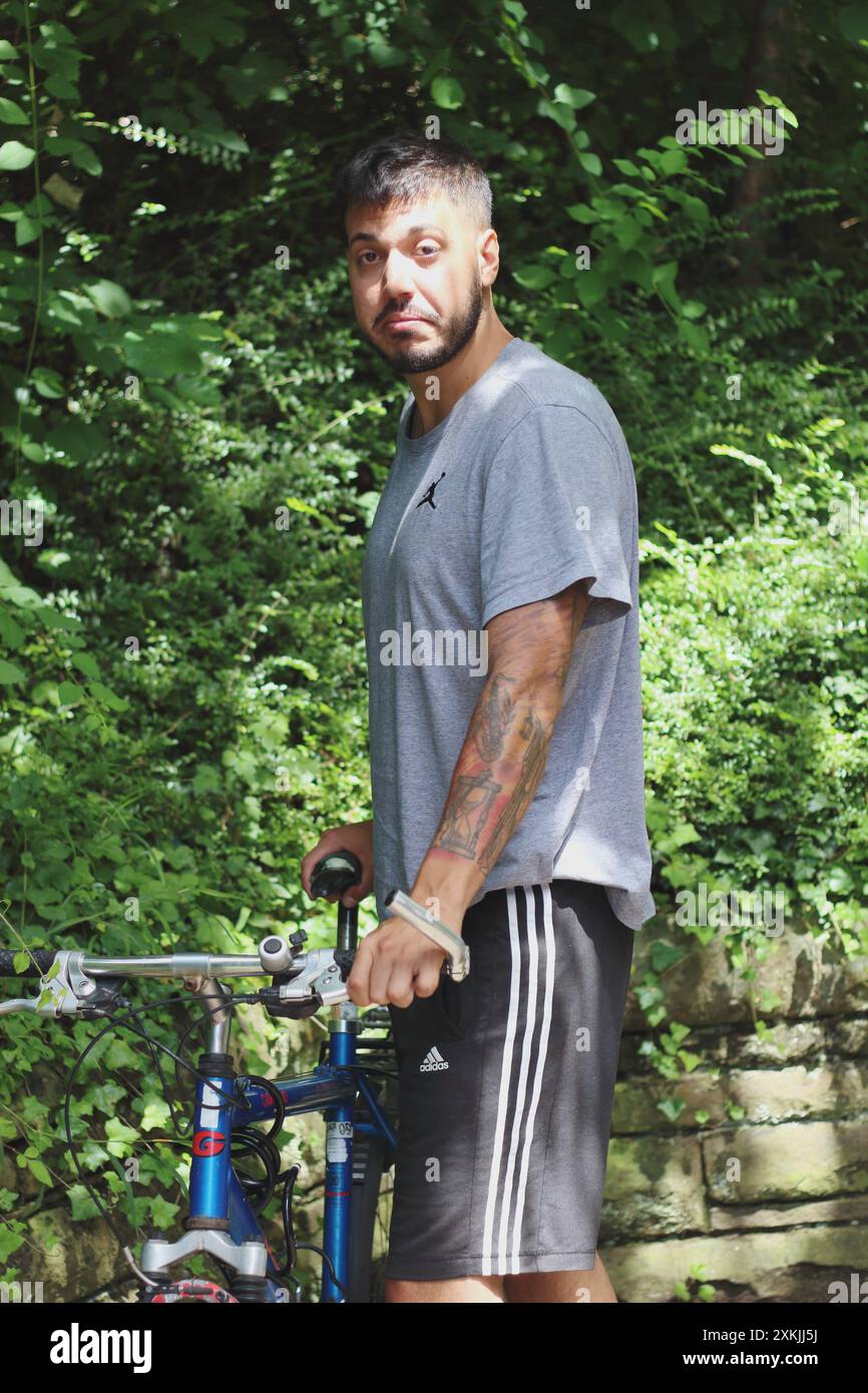 Ein dynamisches Bild, das einen jungen tätowierten Mann aufnimmt, während er sein altes Fahrrad freischaltet. Perfekt für Themen im Zusammenhang mit urbanem Leben, Radfahren und persönlichem Stil Stockfoto