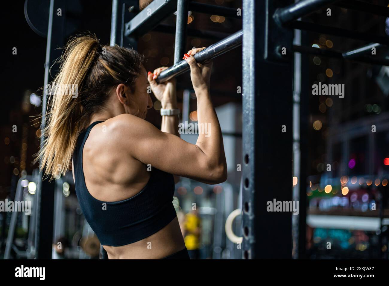 Eine Frau mit einem Pferdeschwanz zieht nachts in einem Fitnessstudio nach. Stockfoto