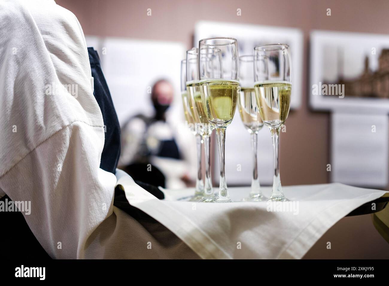 Ein Kellner in einem weißen Hemd und einer schwarzen Schürze hält ein Tablett mit Sektflöten, das sich darauf vorbereitet, die Gäste bei einer formellen Veranstaltung zu servieren. Horizontales Foto Stockfoto