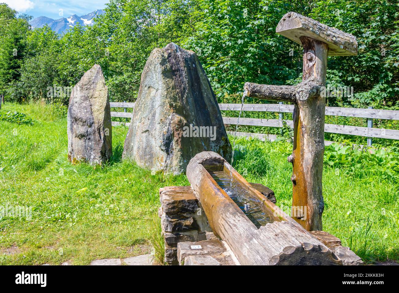 Hölzerne Wassertroge mit Steinmarkierungen, eine lebendige Wasserquelle auf einer Almwiese. Stockfoto