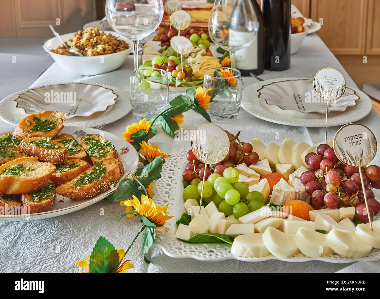 Ein eleganter Shavuot-Feiertagstisch mit Wein, Käse, Obst und Weihnachtsdekoration, bereit für ein traditionelles jüdisches Feiertagsessen. Happy Shavuot Inscript Stockfoto