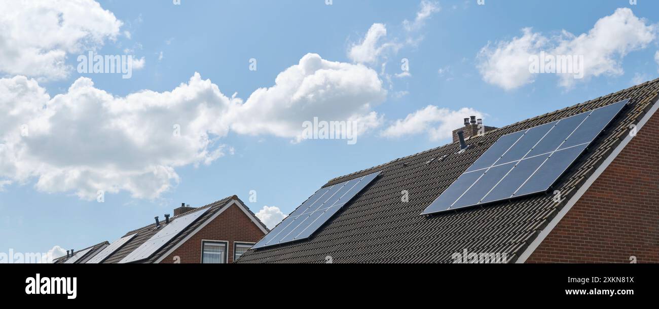 Blaue Solarzellen oder Sonnenkollektoren auf den Dächern von Häusern in einer Reihe, die den blauen bewölkten Himmel reflektieren. Konzept für eine umweltfreundliche nachhaltige Energie Stockfoto
